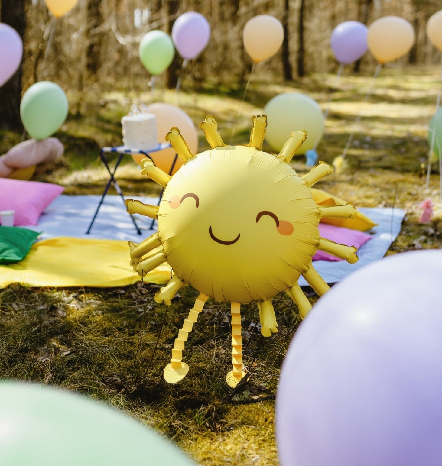 Kids playing outdoors with large foil balloons in shapes of sun, ladybug and bee, forest background
