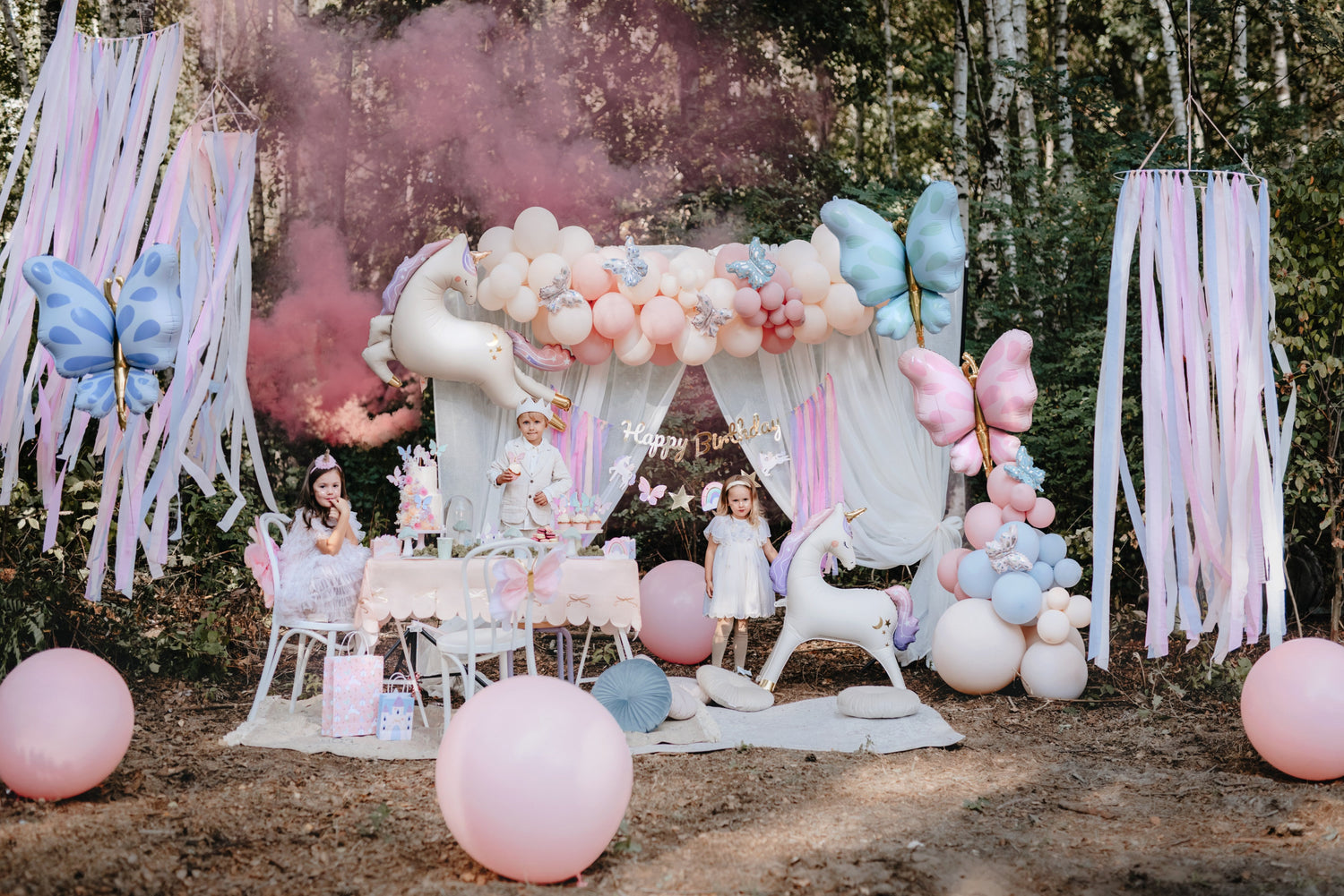 Enchanted unicorn birthday party setup in pastel colors with balloons, butterflies, and forest backdrop