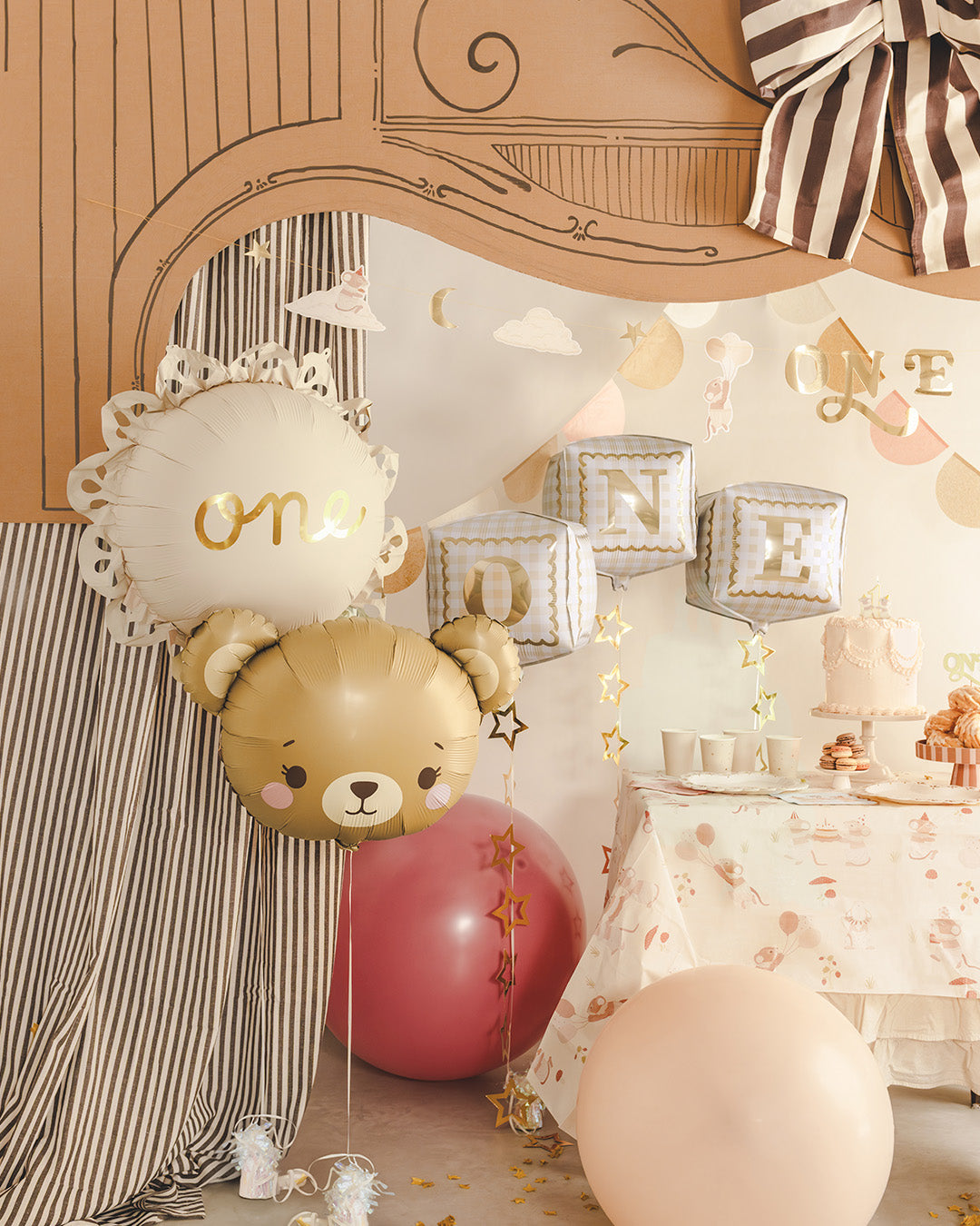 Teddy bear first birthday party decorations with pastel and gold accents, featuring a 'First Birthday' banner, teddy bear balloons, gold star balloons, themed gift bags and a decorated table setup