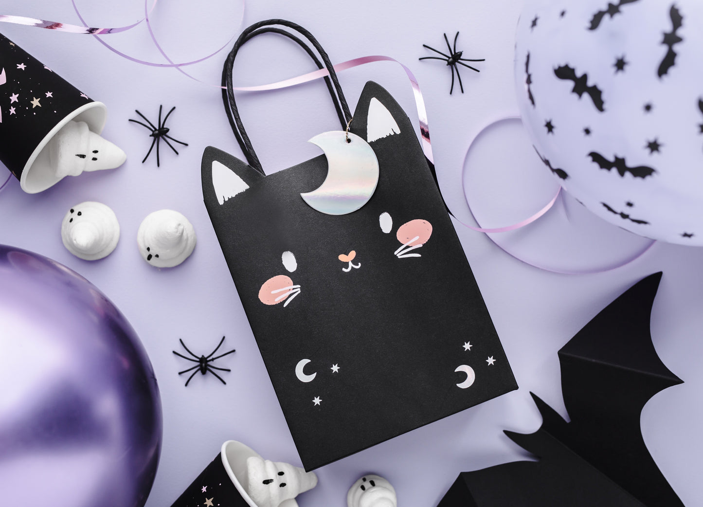 Halloween-themed black cat gift bag with decorative items on a light purple background