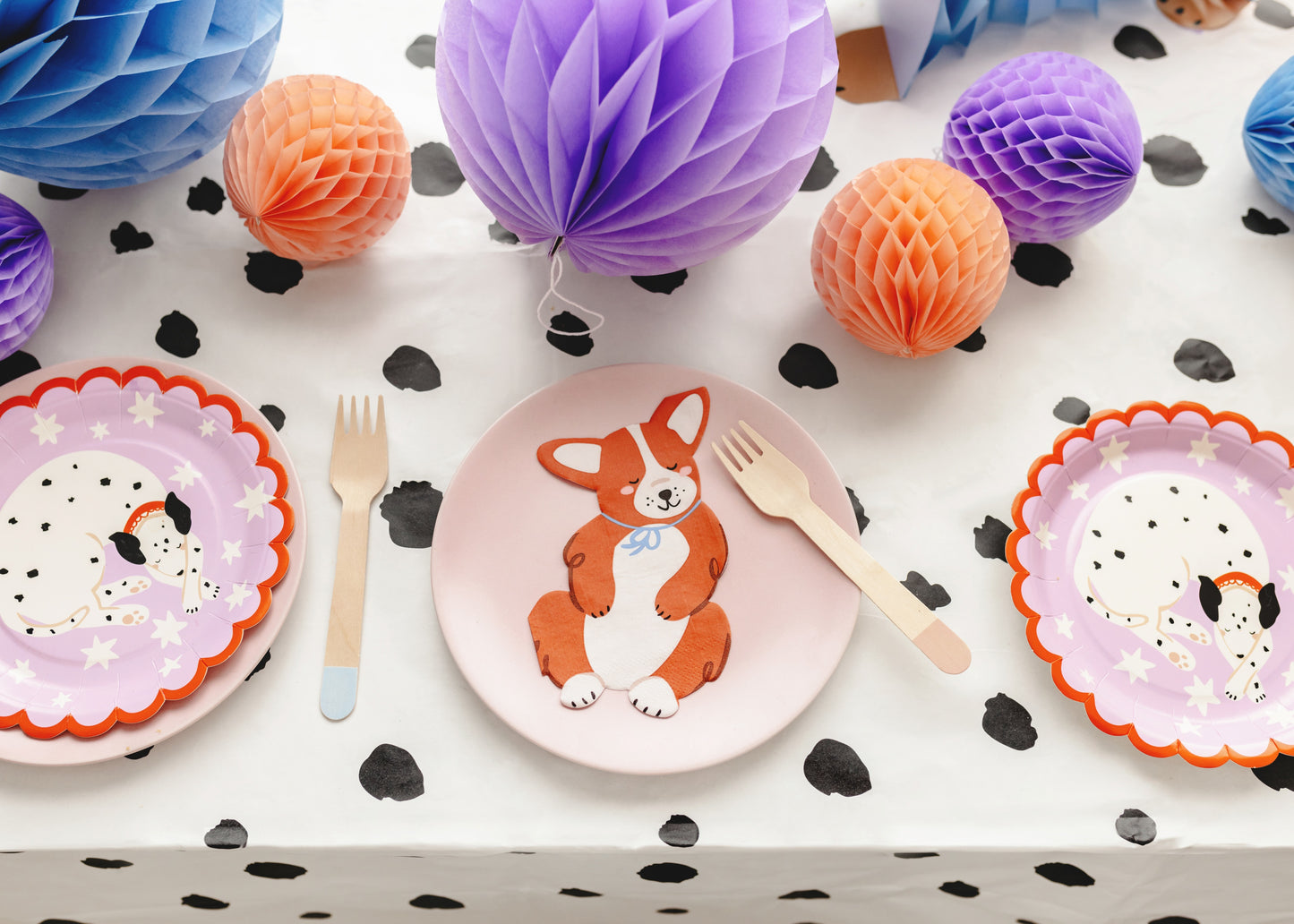Children's plates with animal designs, forks, and decorative paper balls on a polka dot tablecloth.