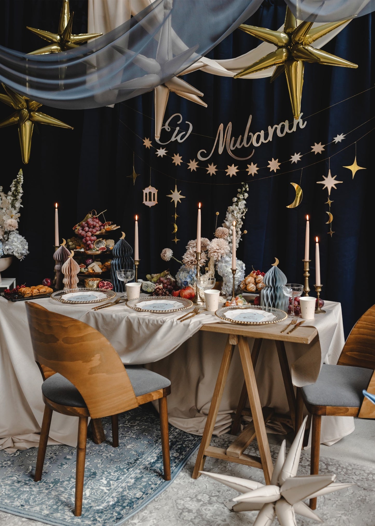 Decorated dining table with 'Eid Mubarak' text, gold stars, and festive decorations against a dark wall.