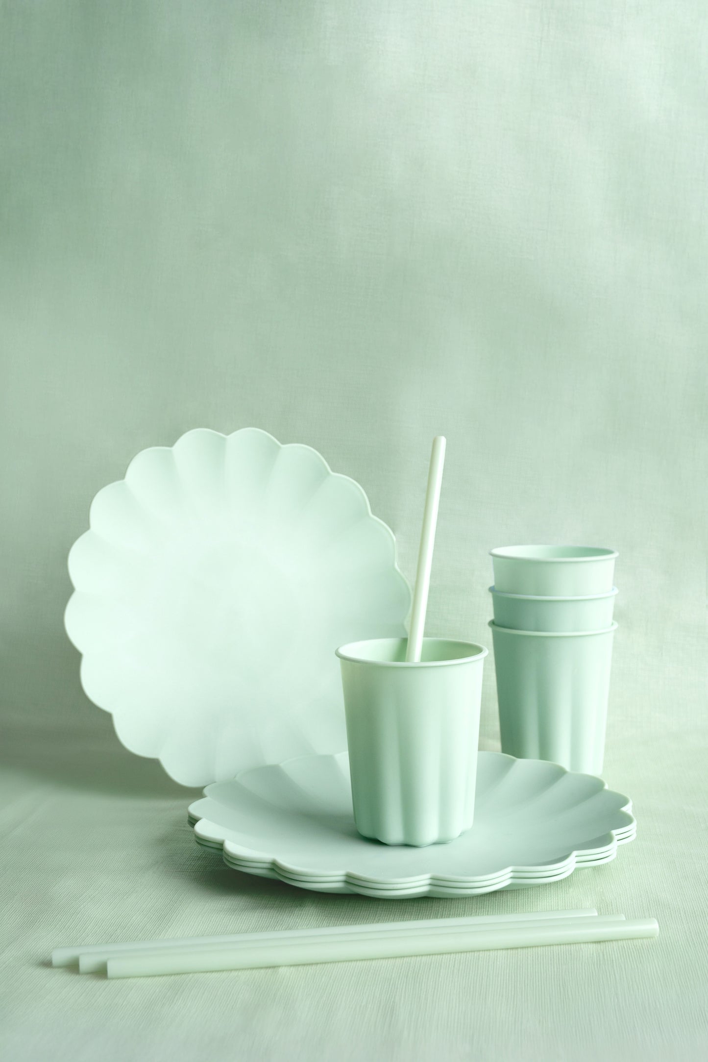 Set of light green plastic plates and cups on a neutral background