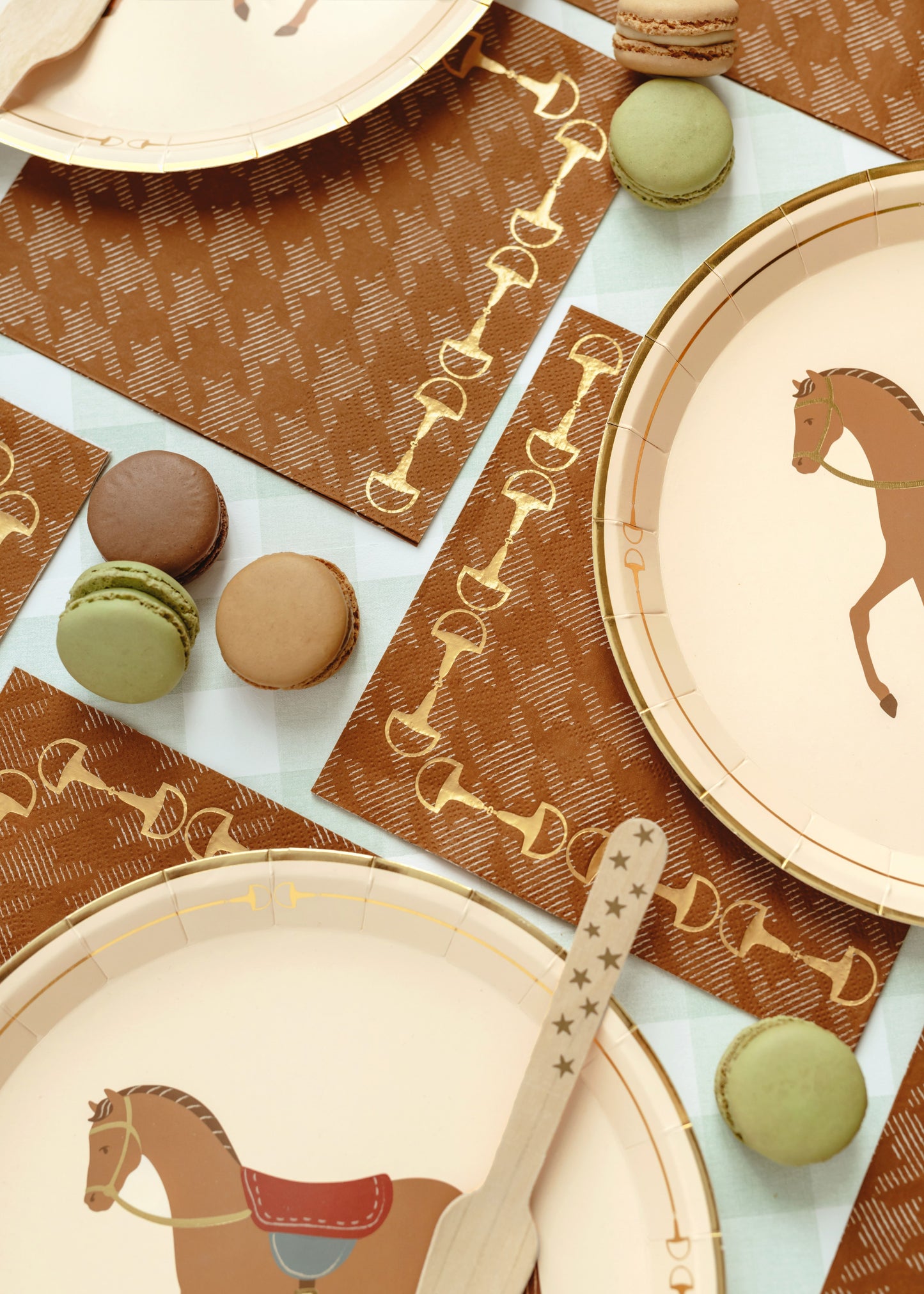 Horse-themed paper plates and brown napkins with bit pattern, surrounded by green and brown macarons – perfect kids’ equestrian birthday party tableware
