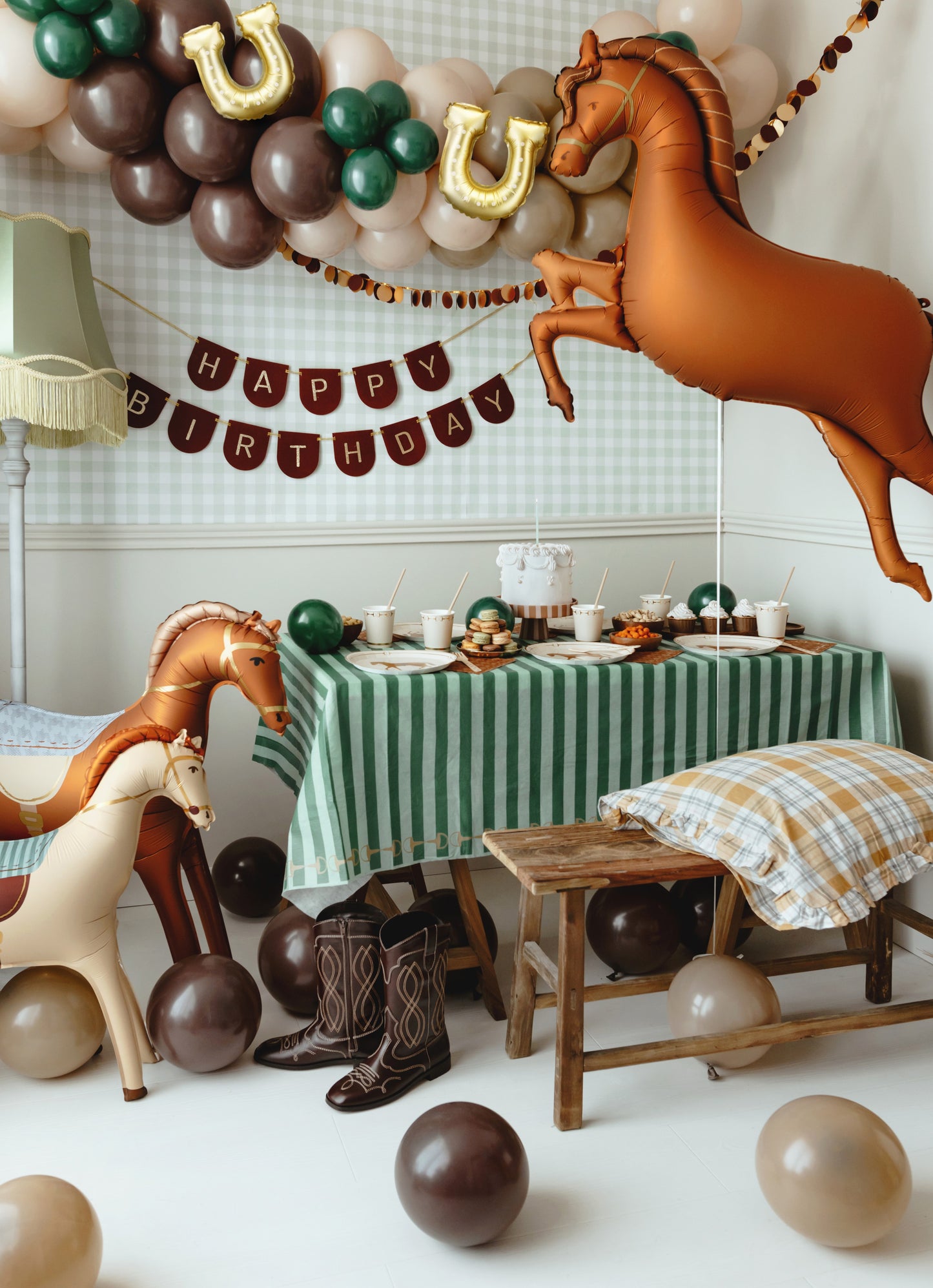 Western horse-themed birthday party setup with inflatable horse balloons, brown and green balloon garland, cowboy boots and rustic tableware