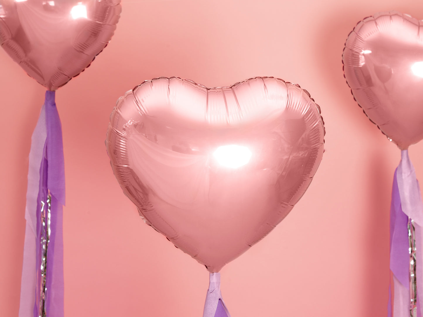 Heart-shaped balloons with ribbons against a pink background