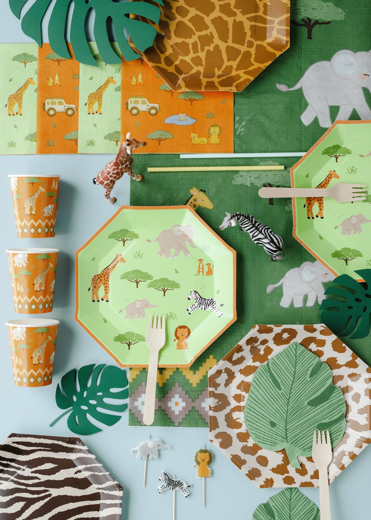 Children's party tableware with safari-themed design on plates, cups, and cutlery.