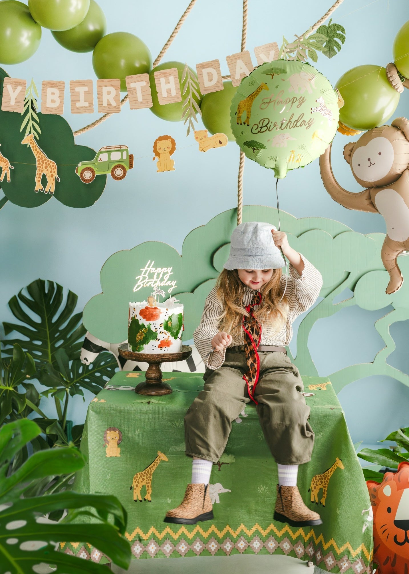 Child at a birthday party with balloons, cake, and safari-themed decorations.