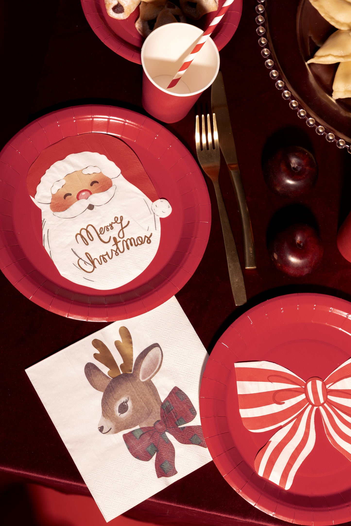 Christmas-themed paper plates with Santa Claus and reindeer designs on a red tablecloth.