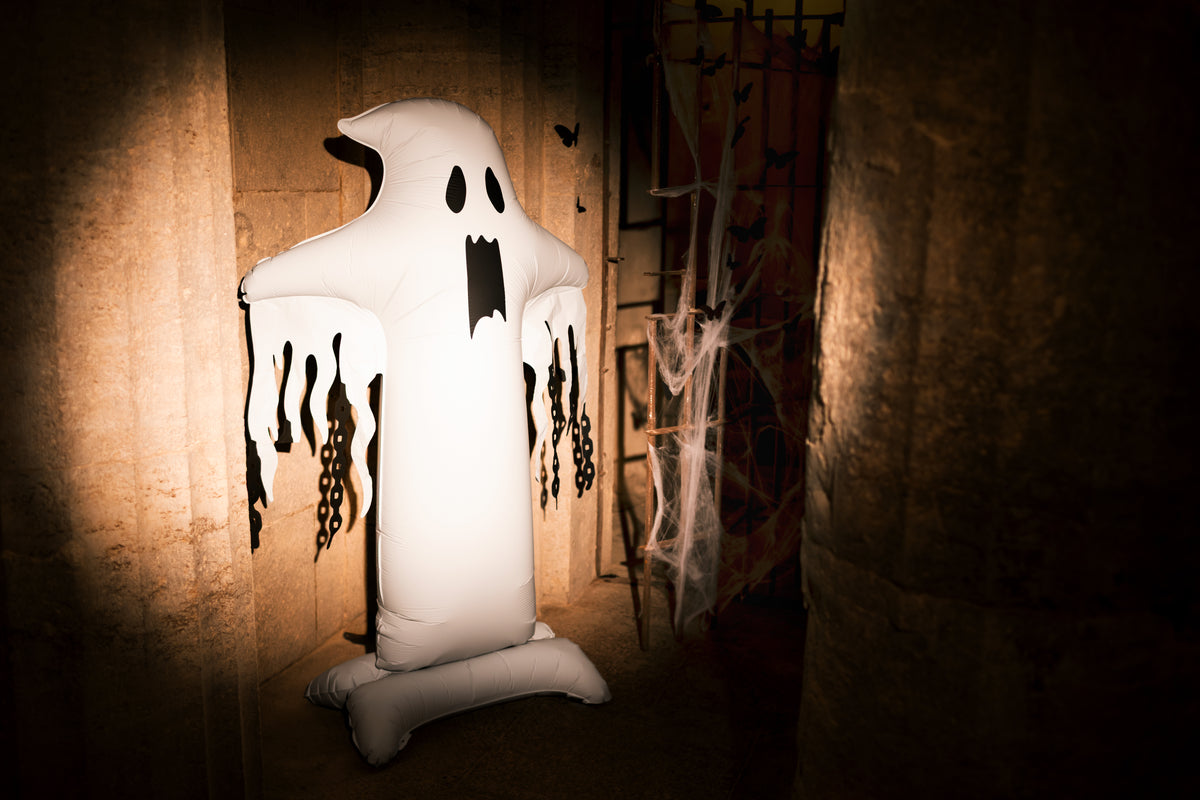 An inflatable white ghost Halloween decoration with black facial features and dripping black details, standing in a dimly lit spooky room setting.