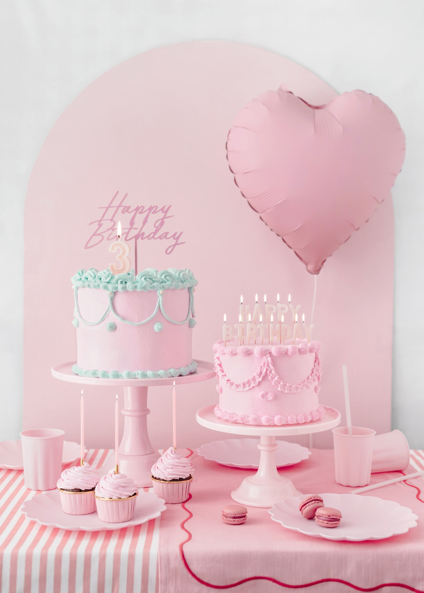 Pink vintage birthday party setup with layered cakes, cupcakes, heart-shaped balloon and pastel pink tableware for a girl’s third birthday