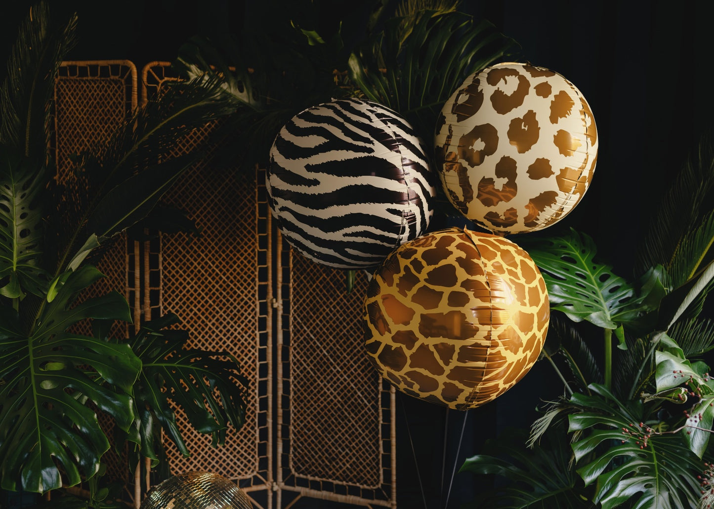 Three spherical balloons with zebra, leopard, and giraffe patterns on a dark background with plants.