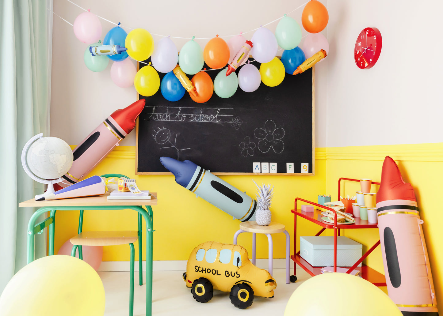 Colorful back to school party setup with pastel balloons, inflatable crayons, school bus decoration, and classroom-themed tableware