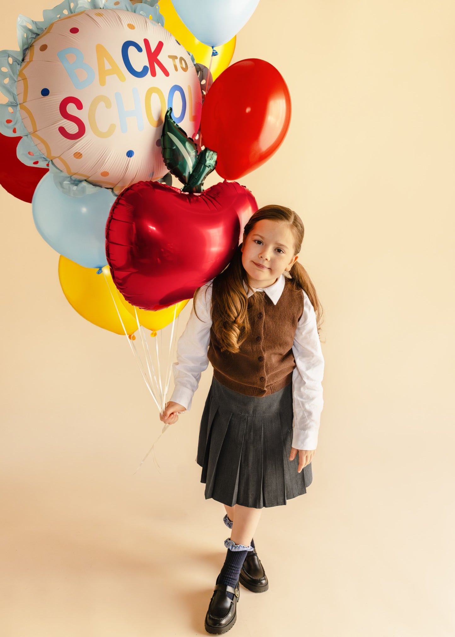 Child holding 'Back to School' balloons with a red apple and a green leaf on a beige background