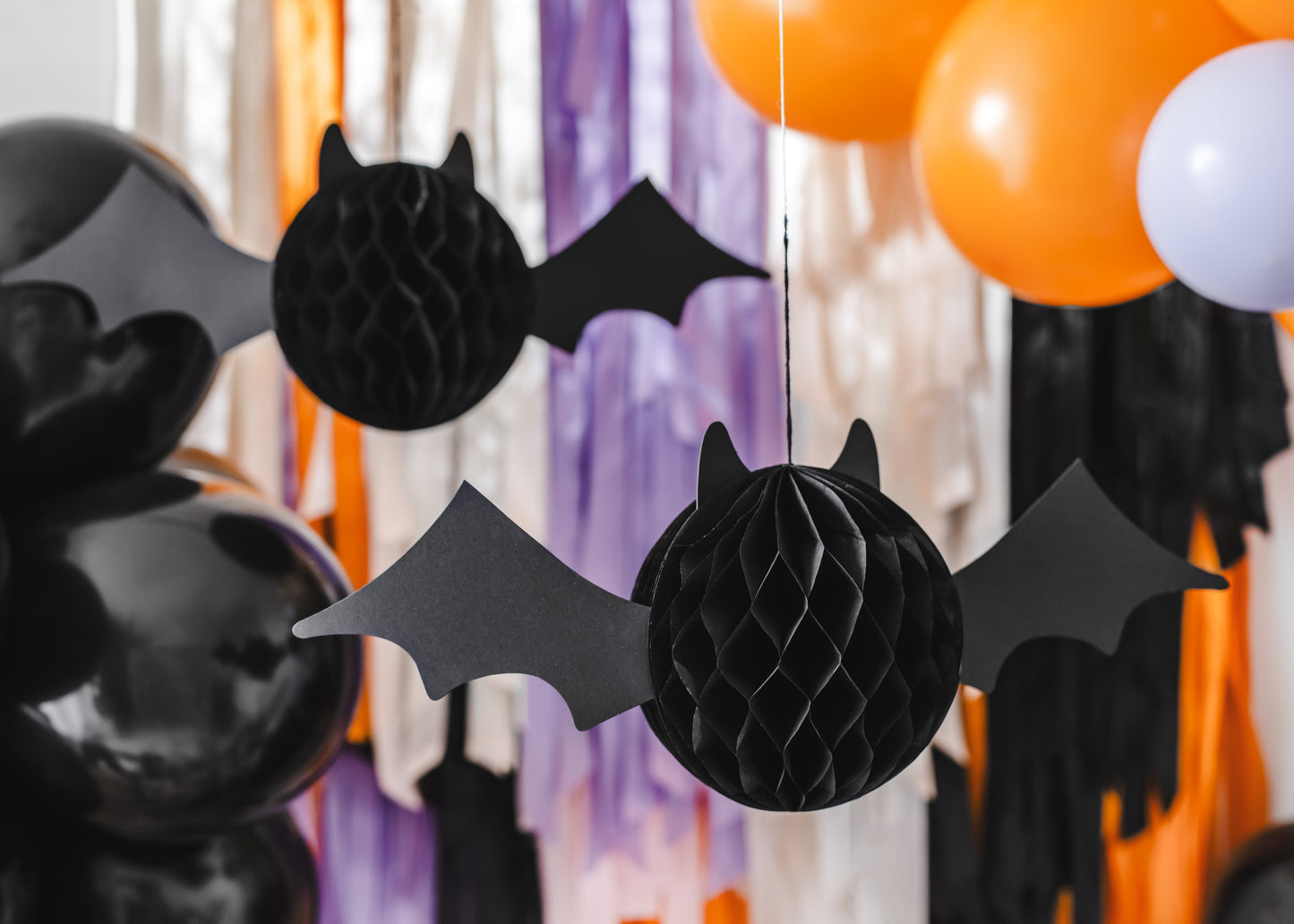 Black bat-shaped decorations hanging against a colorful background with balloons.
