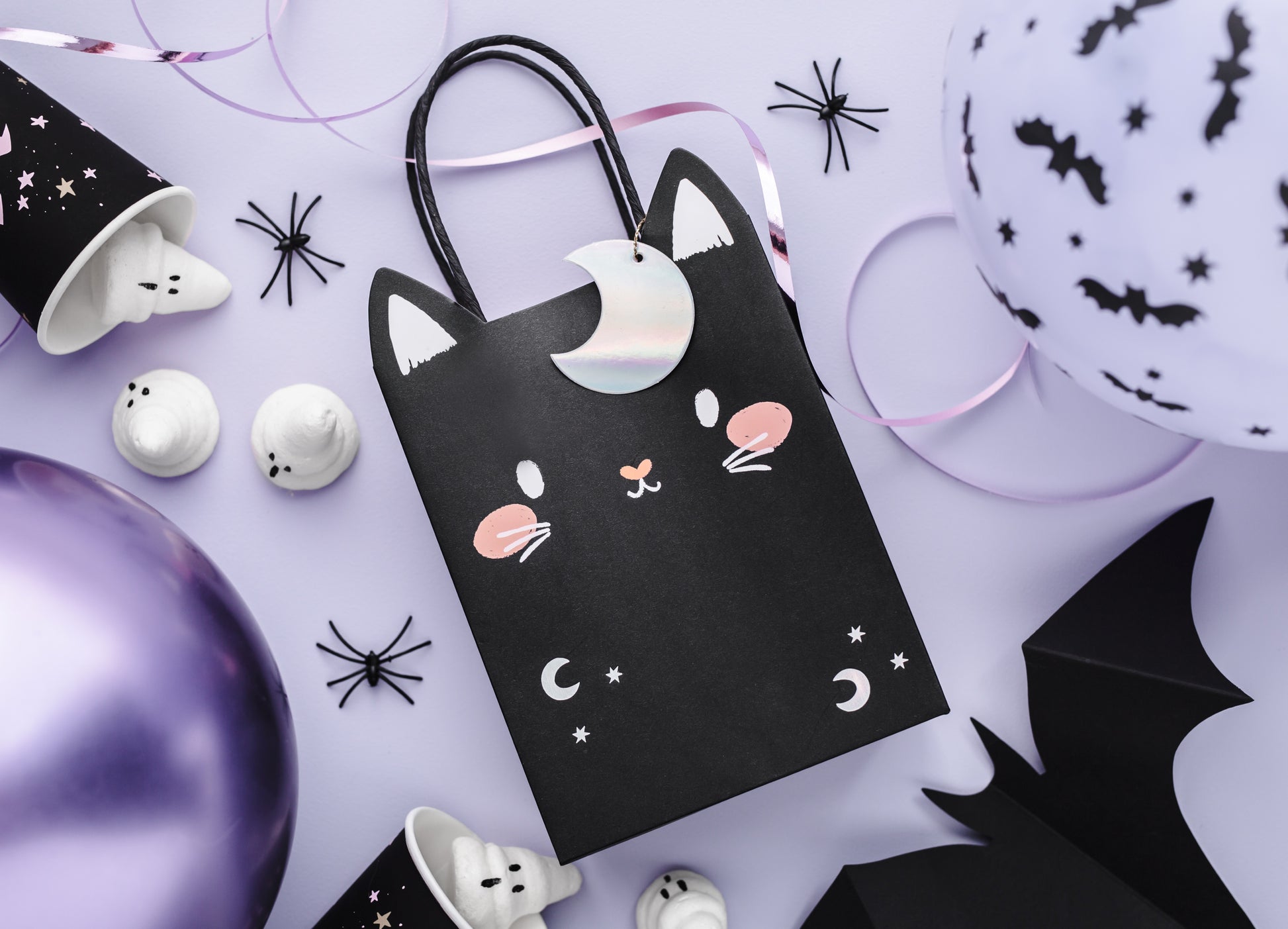 Halloween-themed black cat gift bag with decorative items on a light purple background