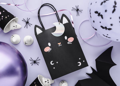 Halloween-themed black cat gift bag with decorative items on a light purple background