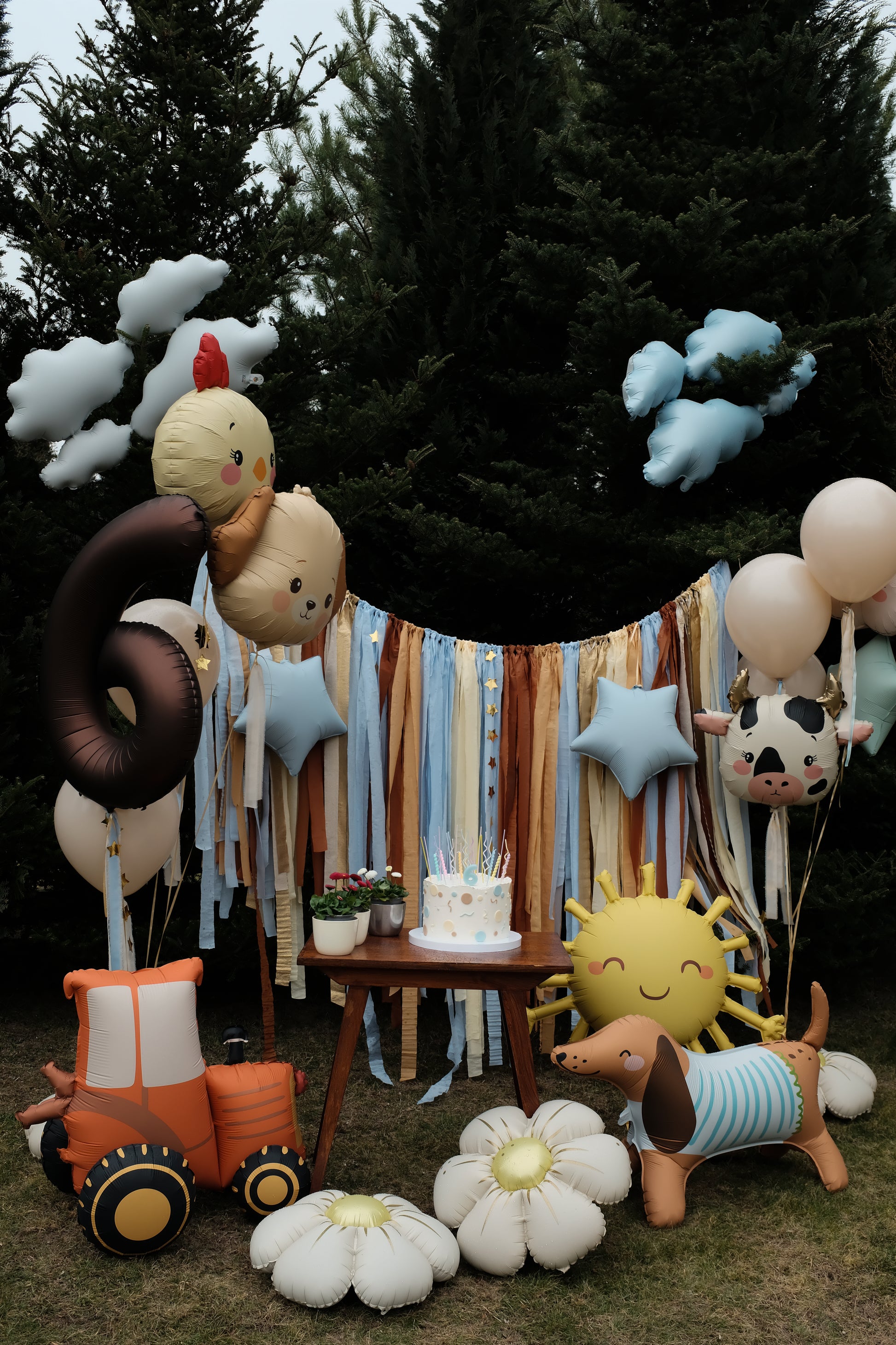 Children's birthday party setup with balloons, a cake, and decorative items under a tree.