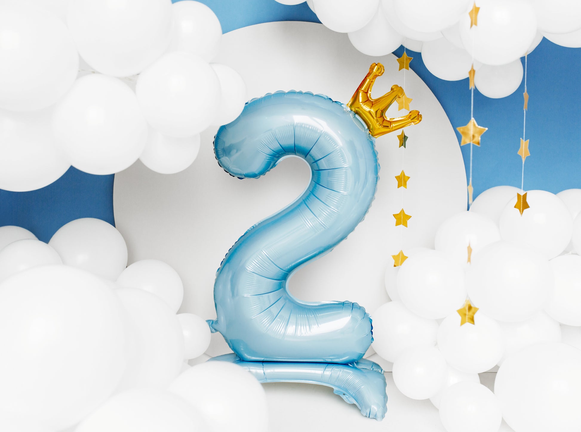 Blue standing number 2 balloon with a crown and stars against a cloud background