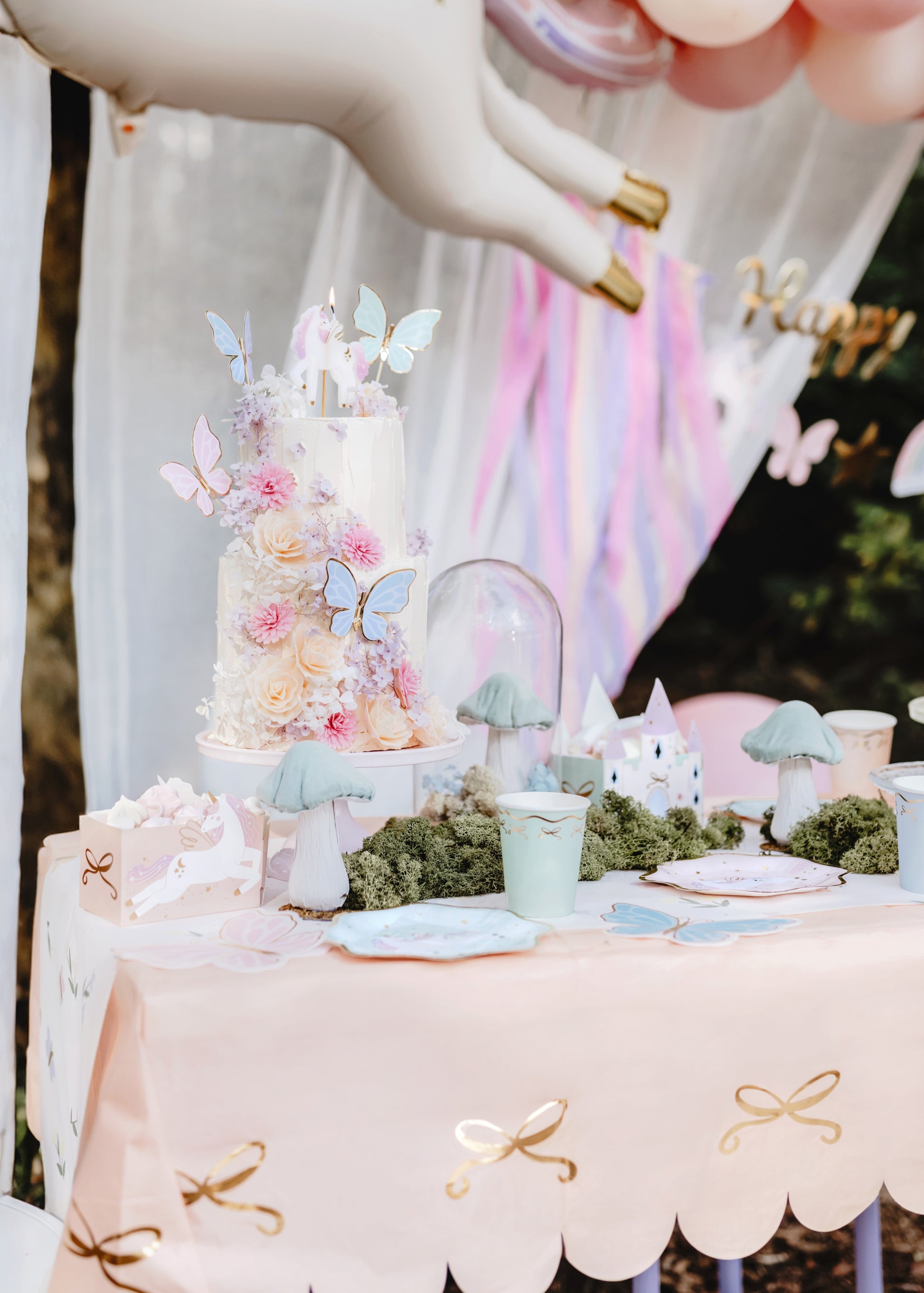 Pastel-colored cake with butterfly decorations on a table with a pink tablecloth.
