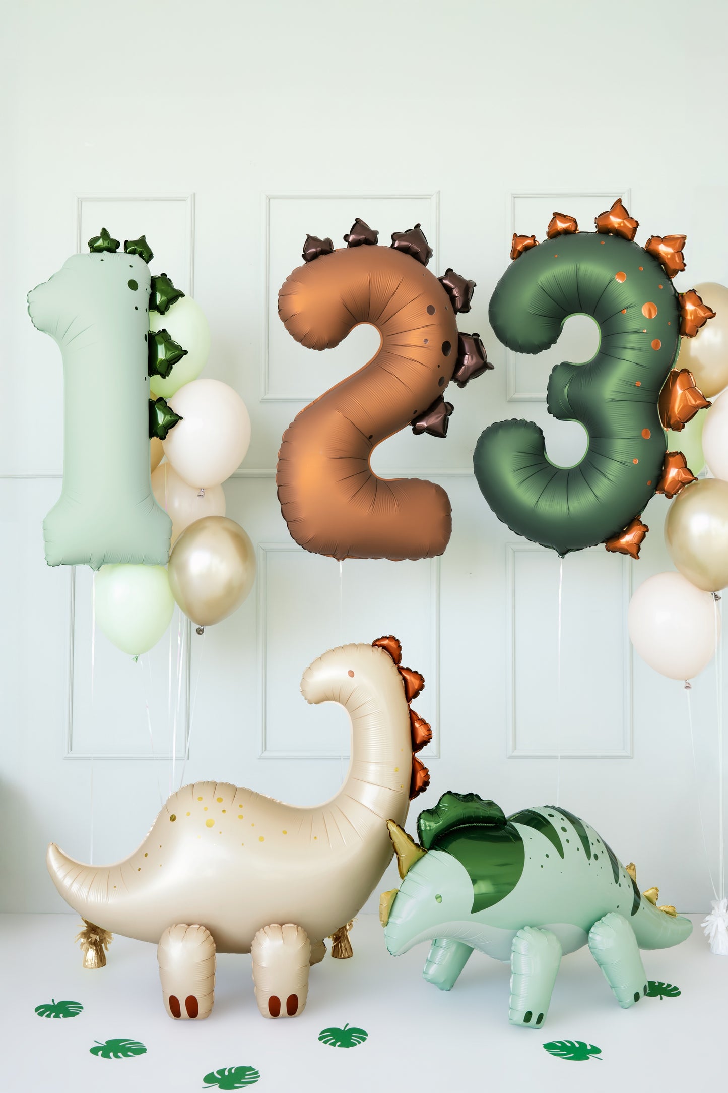 Dinosaur and number-shaped balloons against a white wall with leaf decorations.