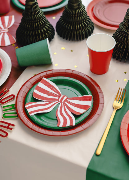 Christmas-themed table setting with red and green plates, festive decorations, and cutlery.