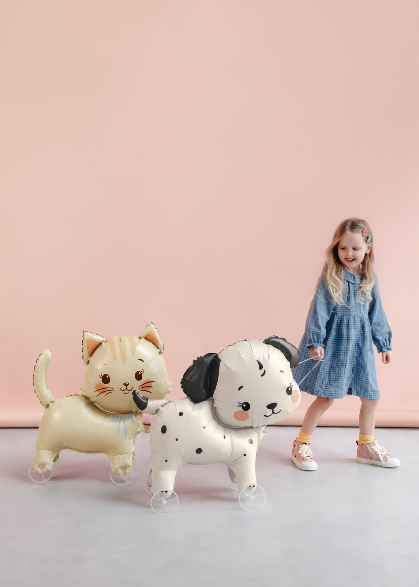 Child with two animal-shaped walking balloons against a pink background