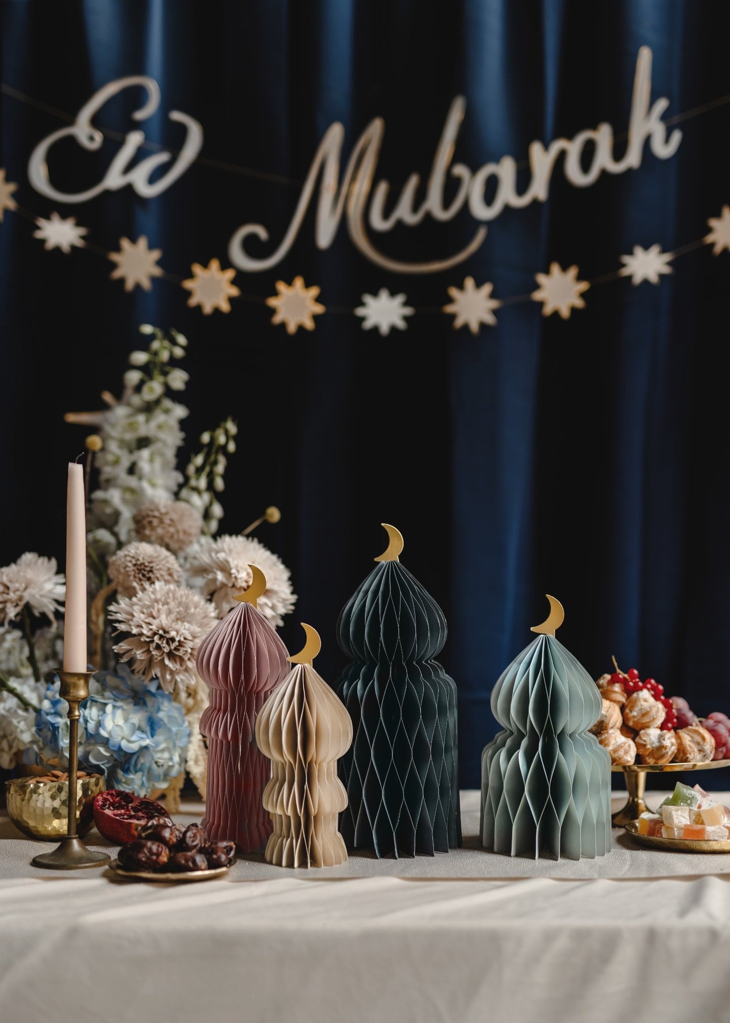 Decorative setup with 'Eid Mubarak' banner, paper lanterns, and floral arrangements on a table.
