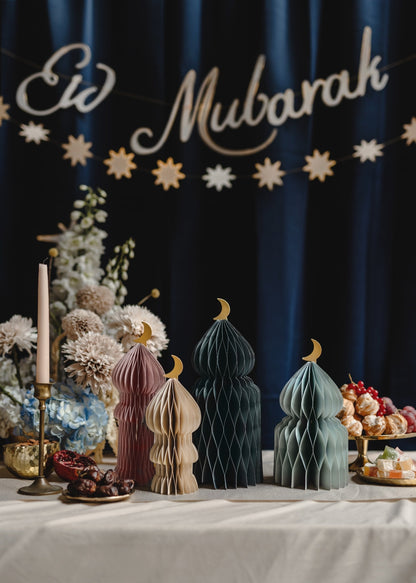 Decorative setup with 'Eid Mubarak' banner, paper lanterns, and floral arrangements on a table.