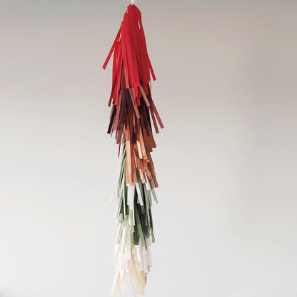 Decorative tassel with red, brown, green, and beige strands on a light gray background