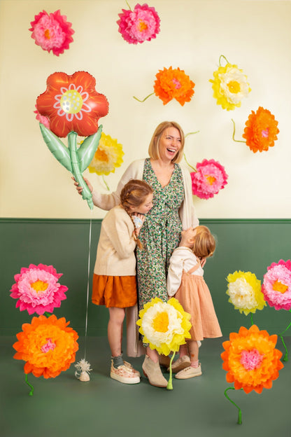Mother and daughters laughing surrounded by colorful flower decorations and holding a flower foil balloon