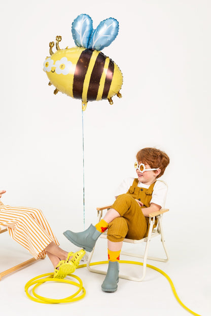Boy sitting on chair with large bee foil balloon, playful spring or summer scene