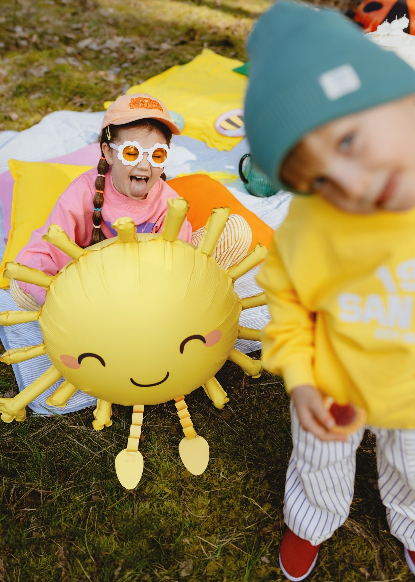 Kids playing outdoors with large foil balloons in shapes of sun, ladybug and bee, forest background
