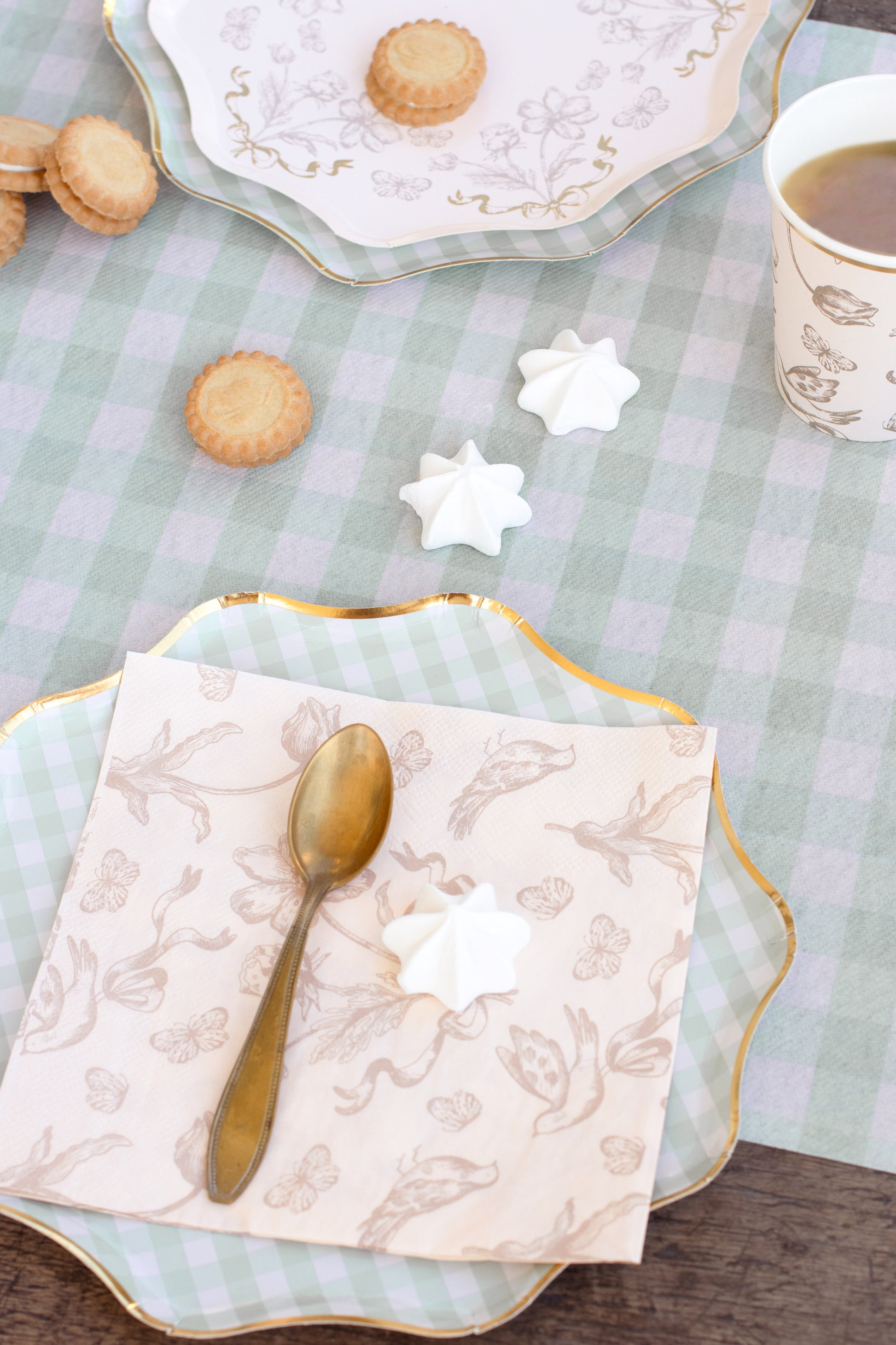Tea set with cookies, star-shaped cookies, and a spoon on a checkered tablecloth.