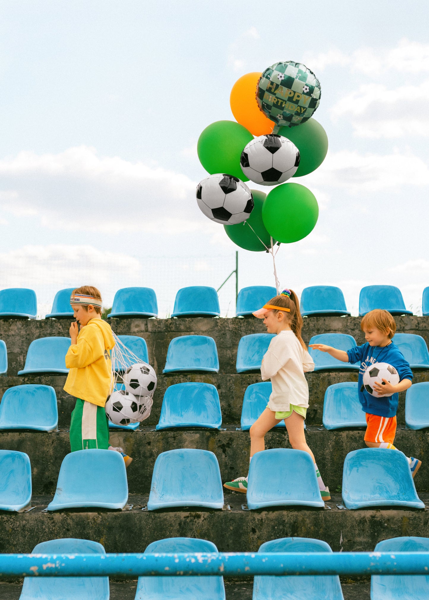Children with soccer-themed balloons and balls in a stadium setting