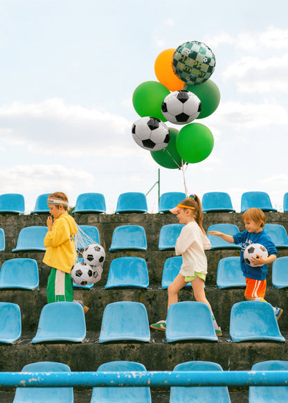 Children with soccer-themed balloons and balls in a stadium setting