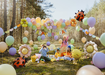 Colorful outdoor kids birthday party with pastel balloon garland, daisy flower balloons, sun and ladybug foil balloons, and happy children celebrating in a forest setting