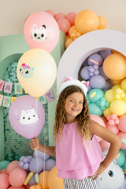 Young girl holding a balloon with a cat design in front of a colorful balloon arch.