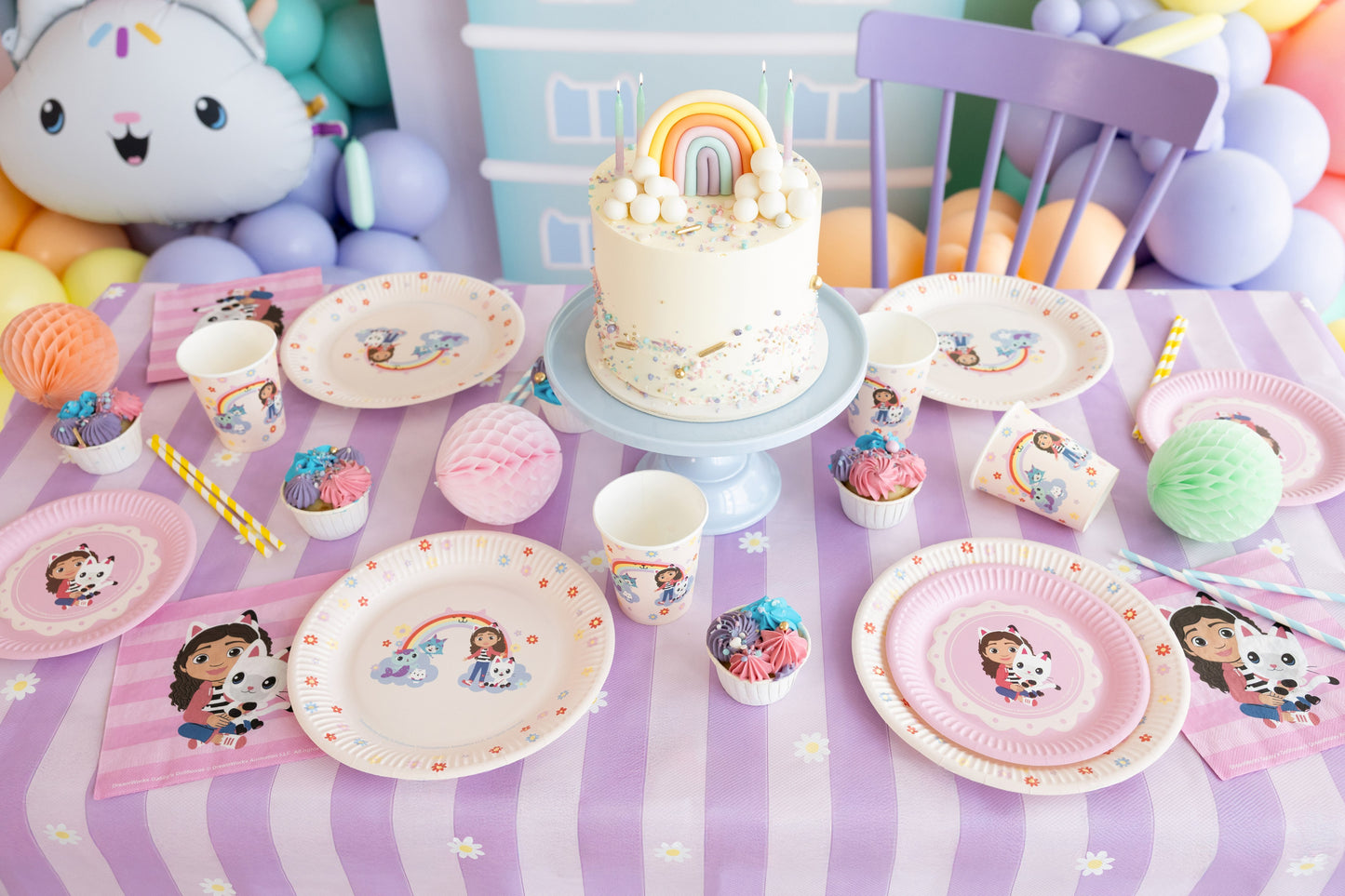 Children's birthday party setup with cake, plates, and decorations on a tablecloth.