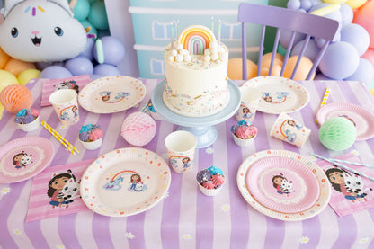 Children's birthday party setup with cake, plates, and decorations on a tablecloth.