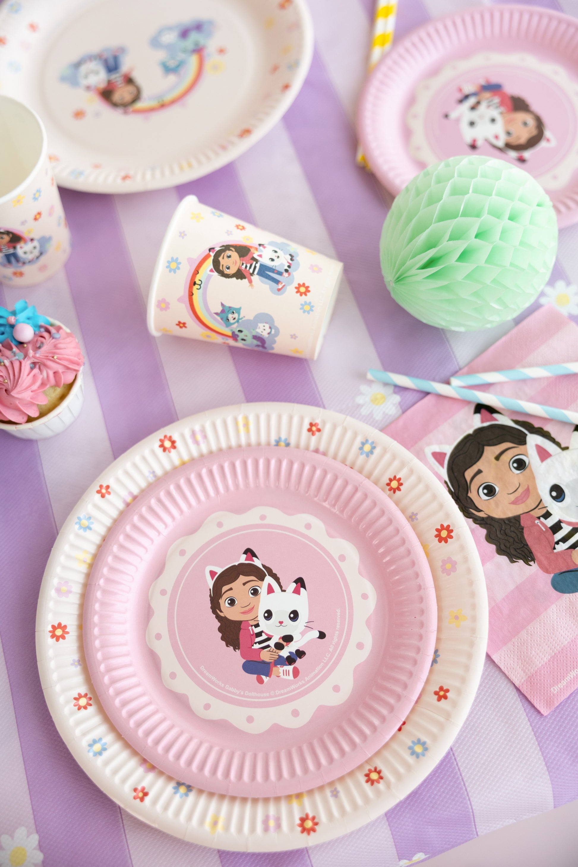 Children's party tableware with plates, cups, and napkins featuring cartoon characters on a purple surface.