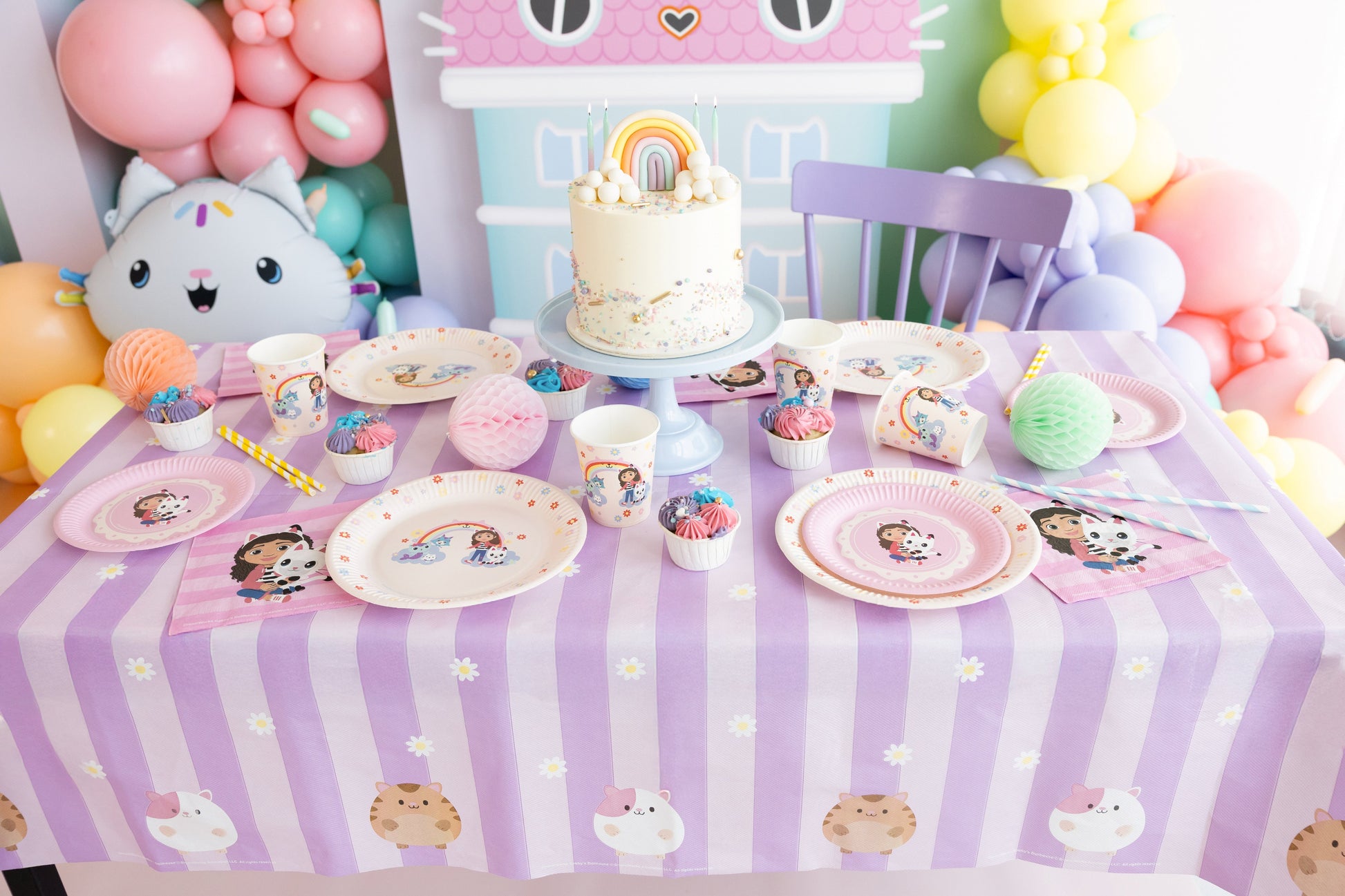 Children's birthday party setup with a cake, plates, and balloons on a table.