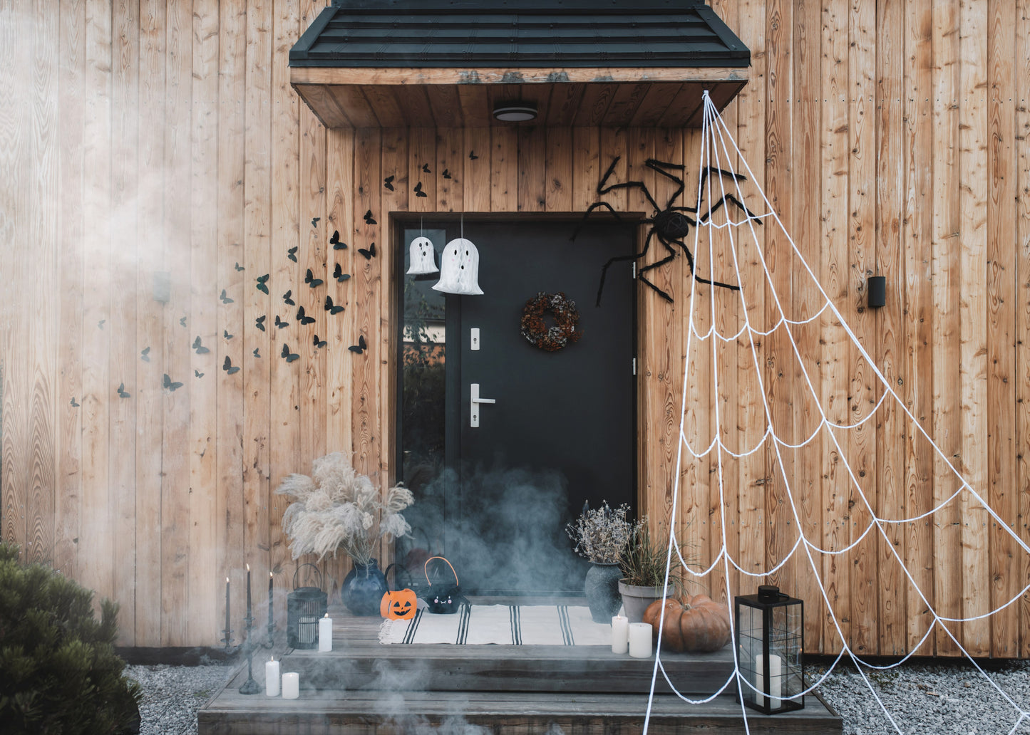 Halloween-themed outdoor decoration with spider webs, ghosts, and pumpkins on a wooden house.