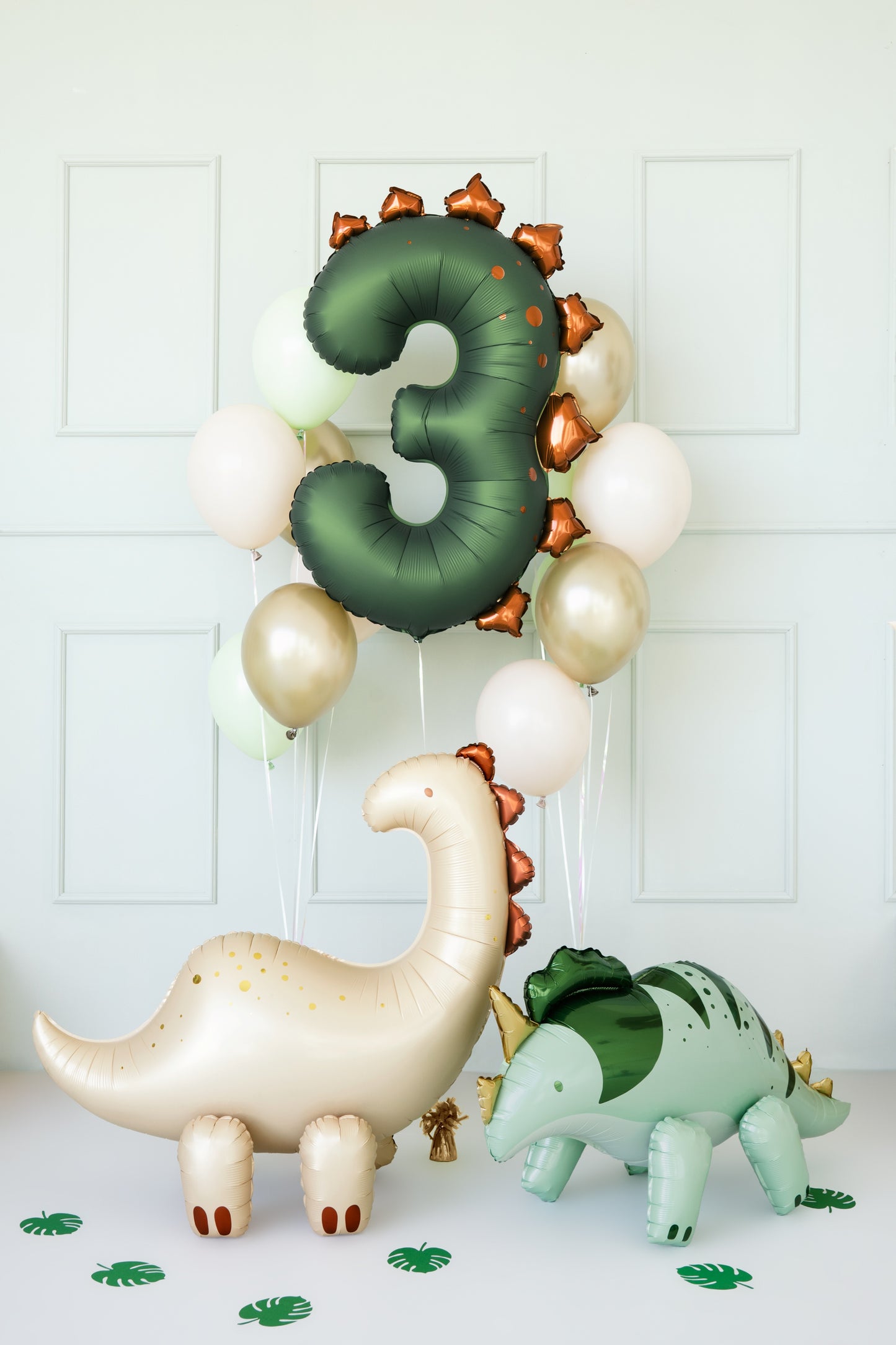 Decorative balloon arch with dinosaur balloons and number '3' against a white wall.
