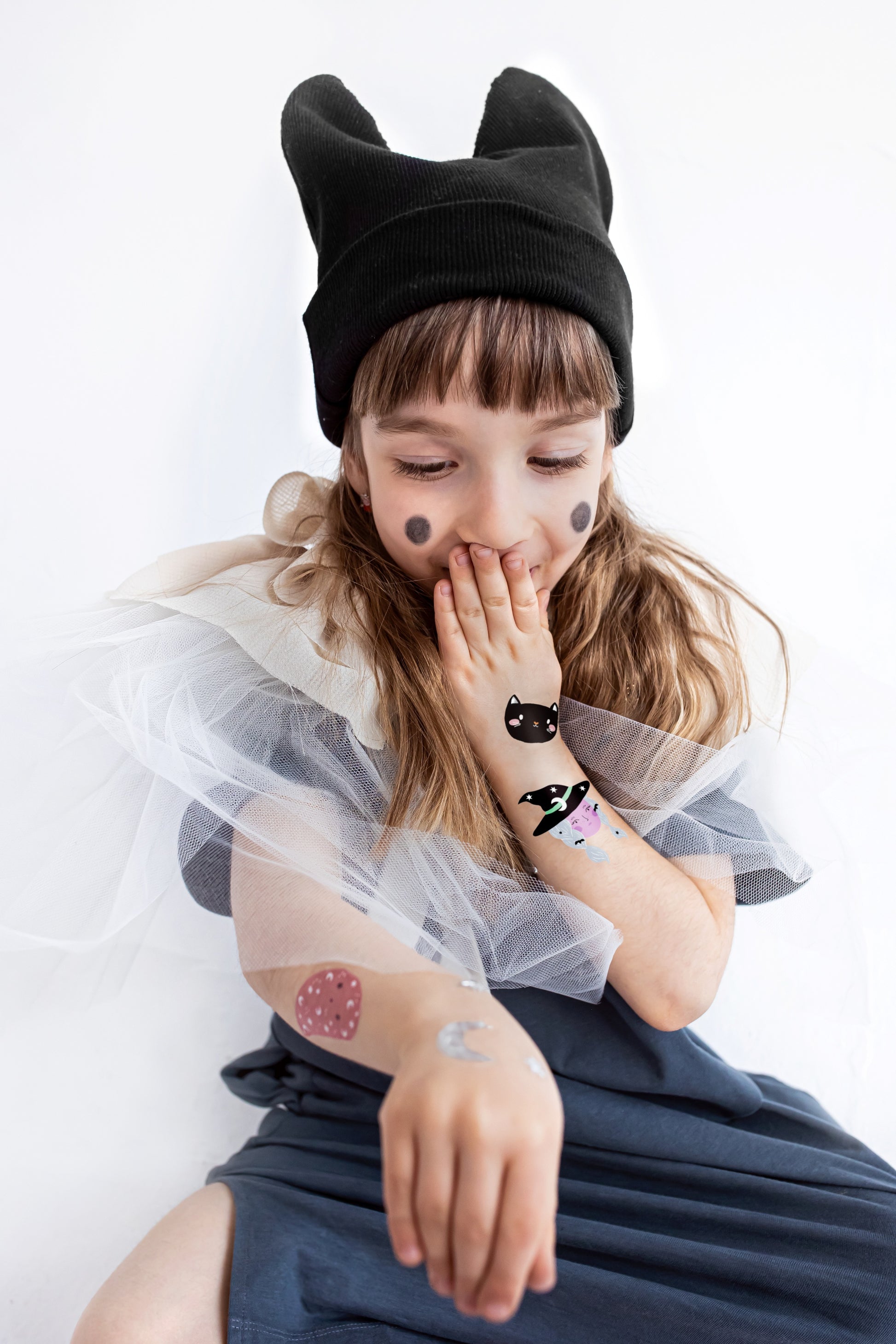 Child wearing a black cat-themed hat with ears, sitting on a white background