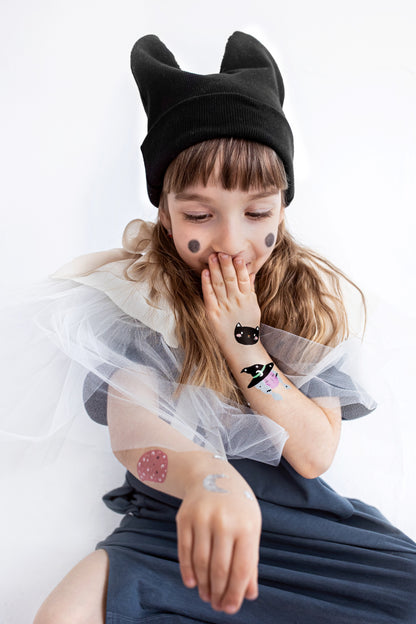 Child wearing a black cat-themed hat with ears, sitting on a white background