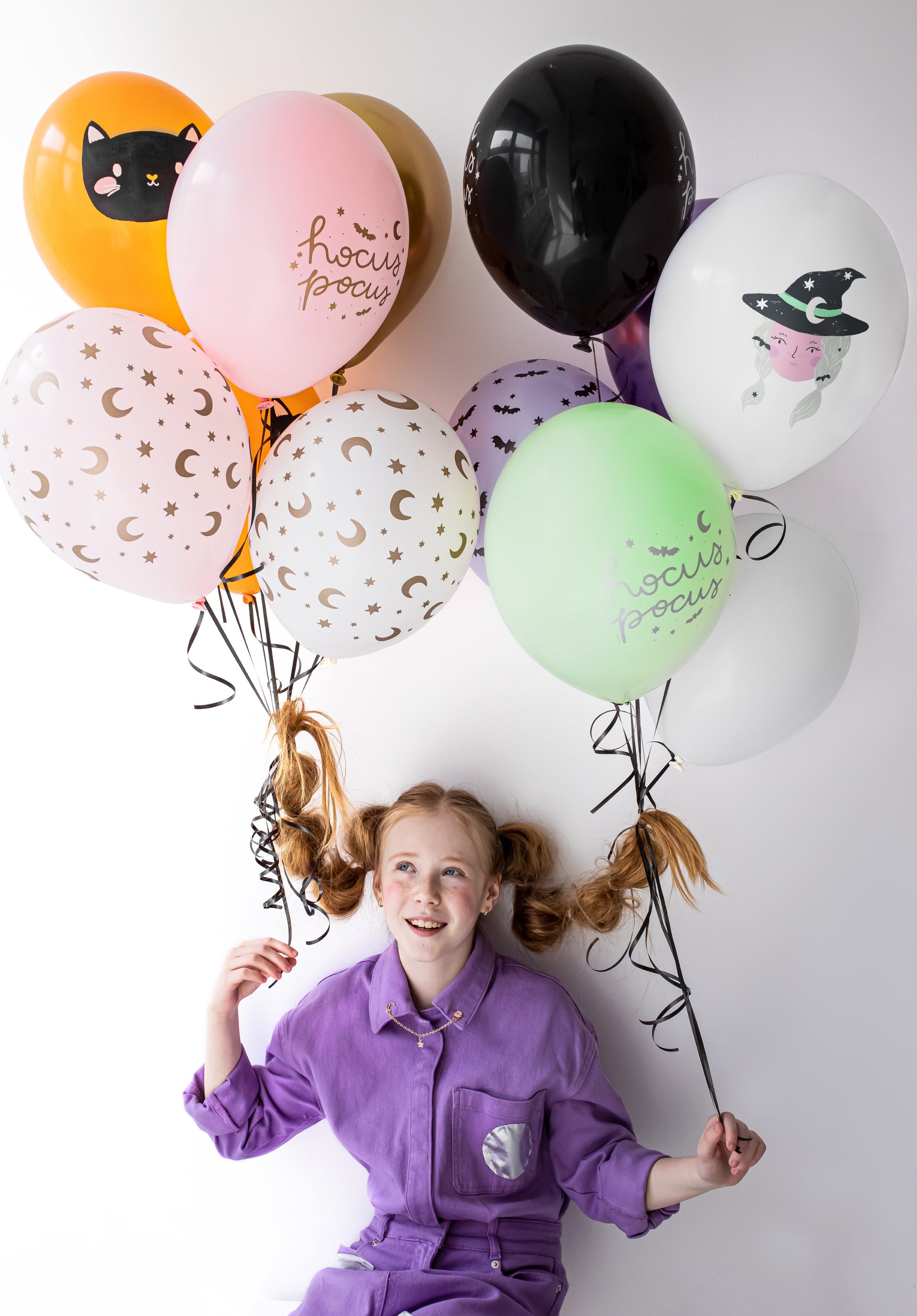 Person holding colorful balloons with Halloween designs on a white background