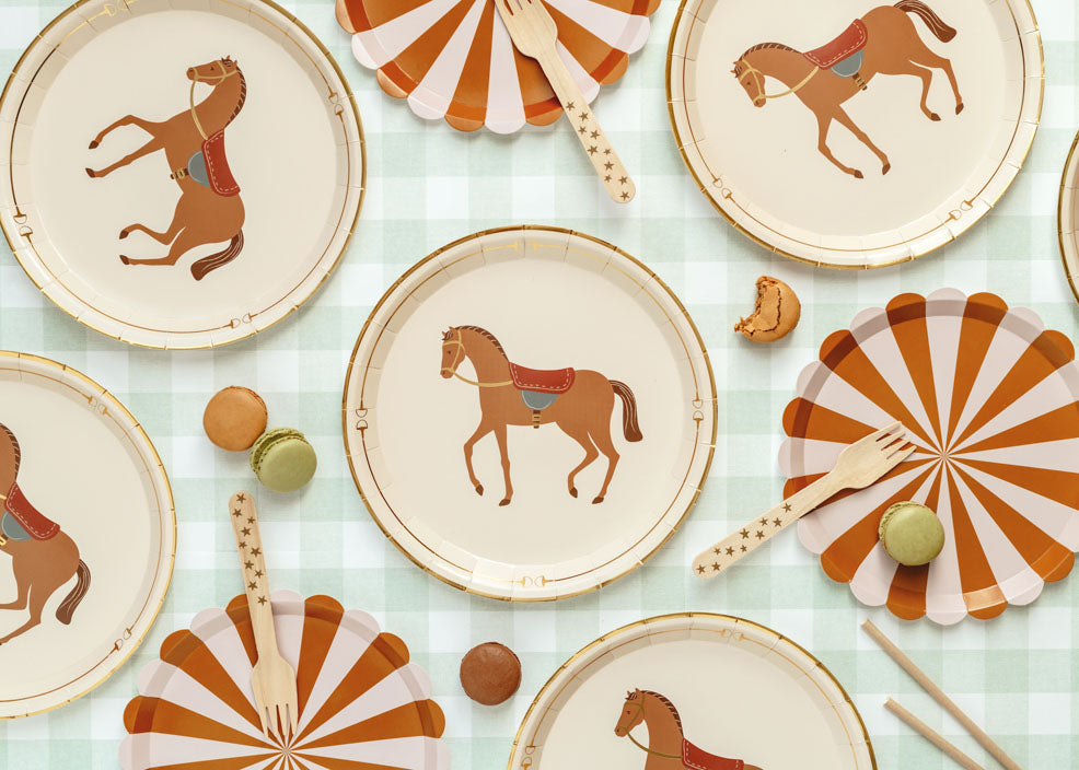 Horse-themed party paper plates with saddle illustrations, paired with orange striped plates, star-print wooden forks, and assorted macarons – kids’ equestrian birthday table setting