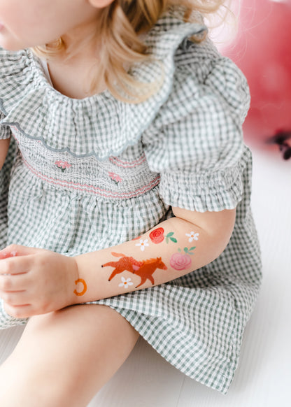 Child with temporary tattoos on their arm, wearing a checkered dress.
