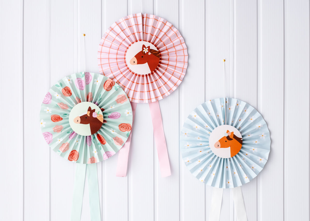 Three colorful paper fans with horse designs on a white wooden background
